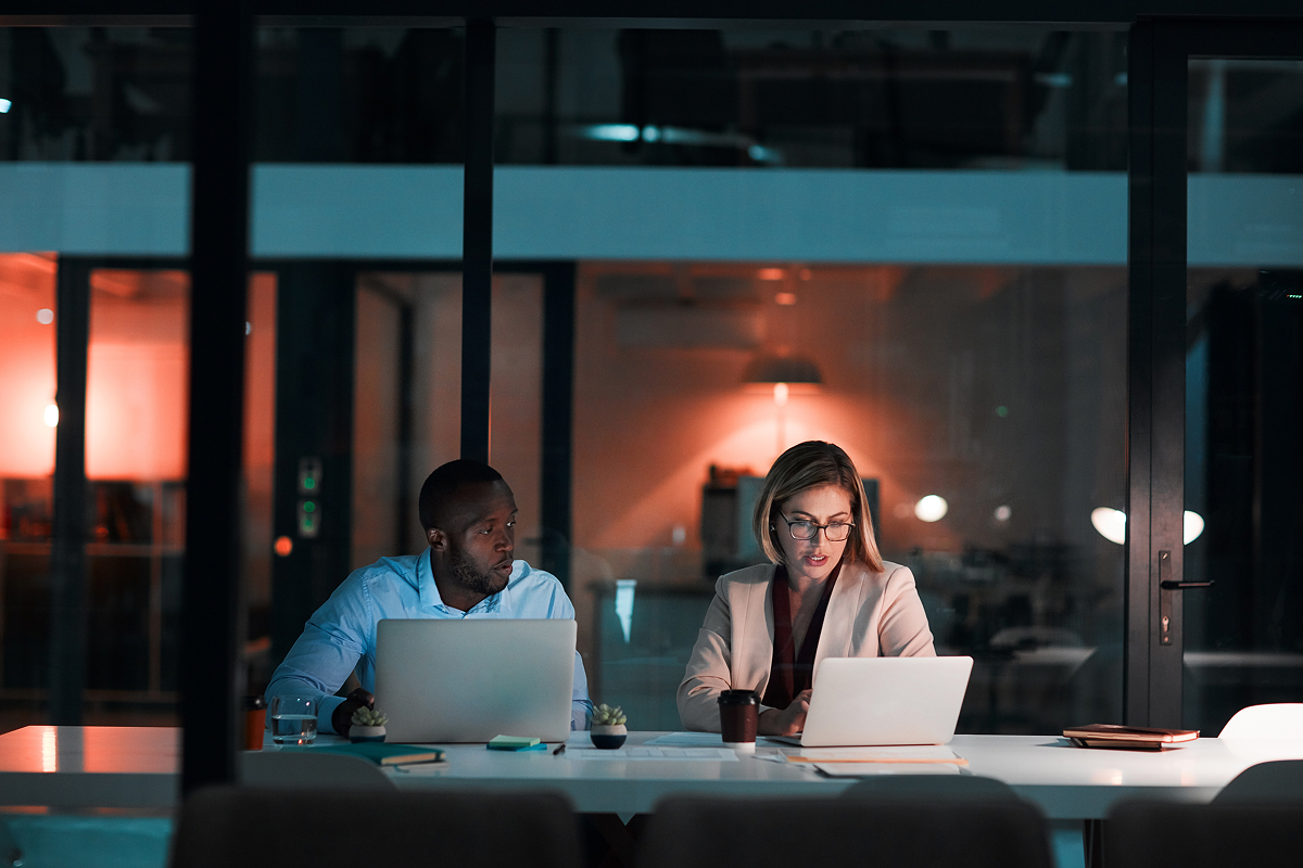 Man and woman in an office sitting at a tabling working on laptops